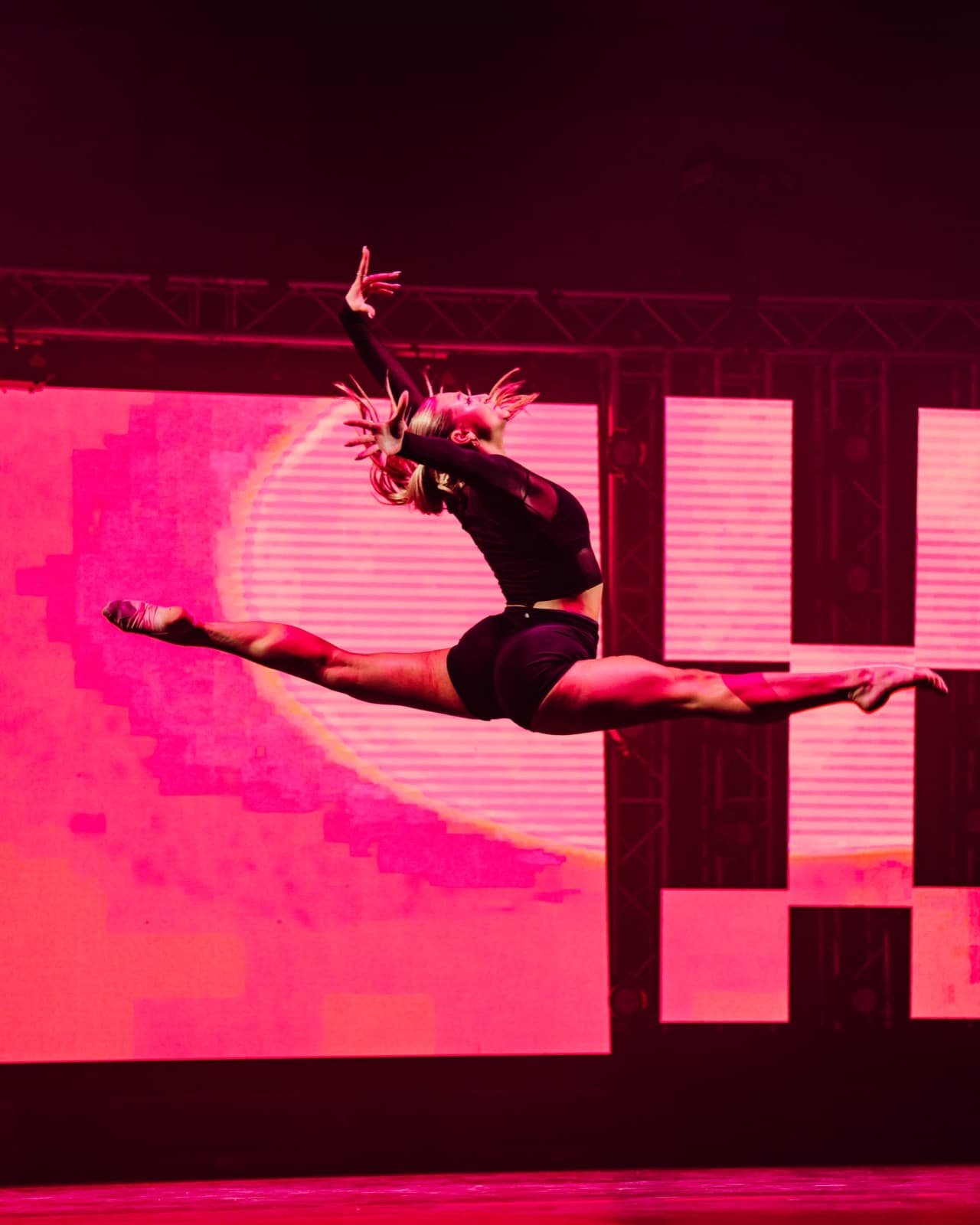 Five World aerial performer suspended in front of magenta LED stage visuals.
