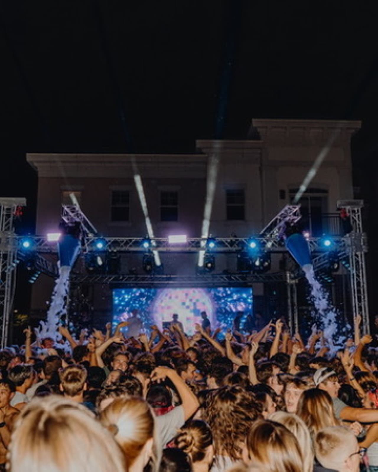 Private party stage with blue lighting, haze, and performers in front of a crowd.