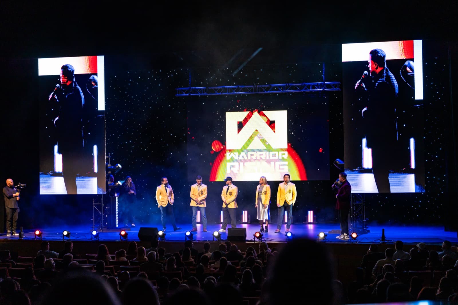 Warrior Rising gala stage with presenter and wide video screen.