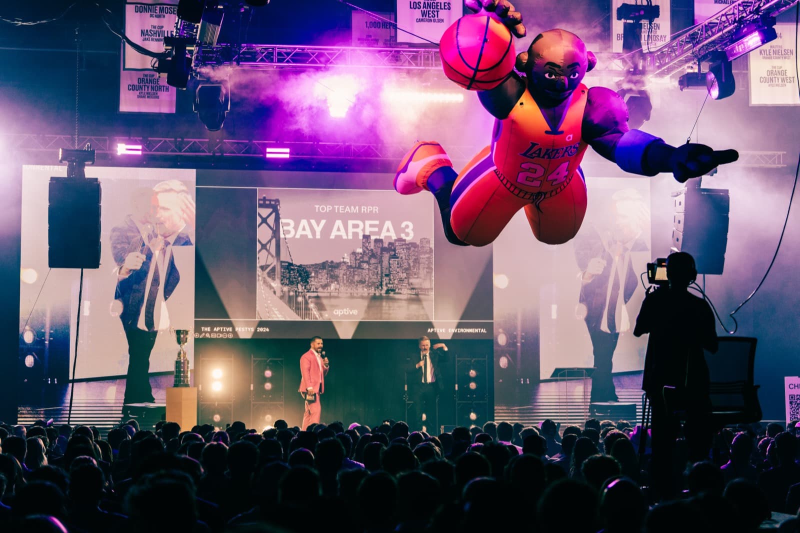 Aptive awards show stage with bright magenta lighting and performers silhouetted in front of LED screens.