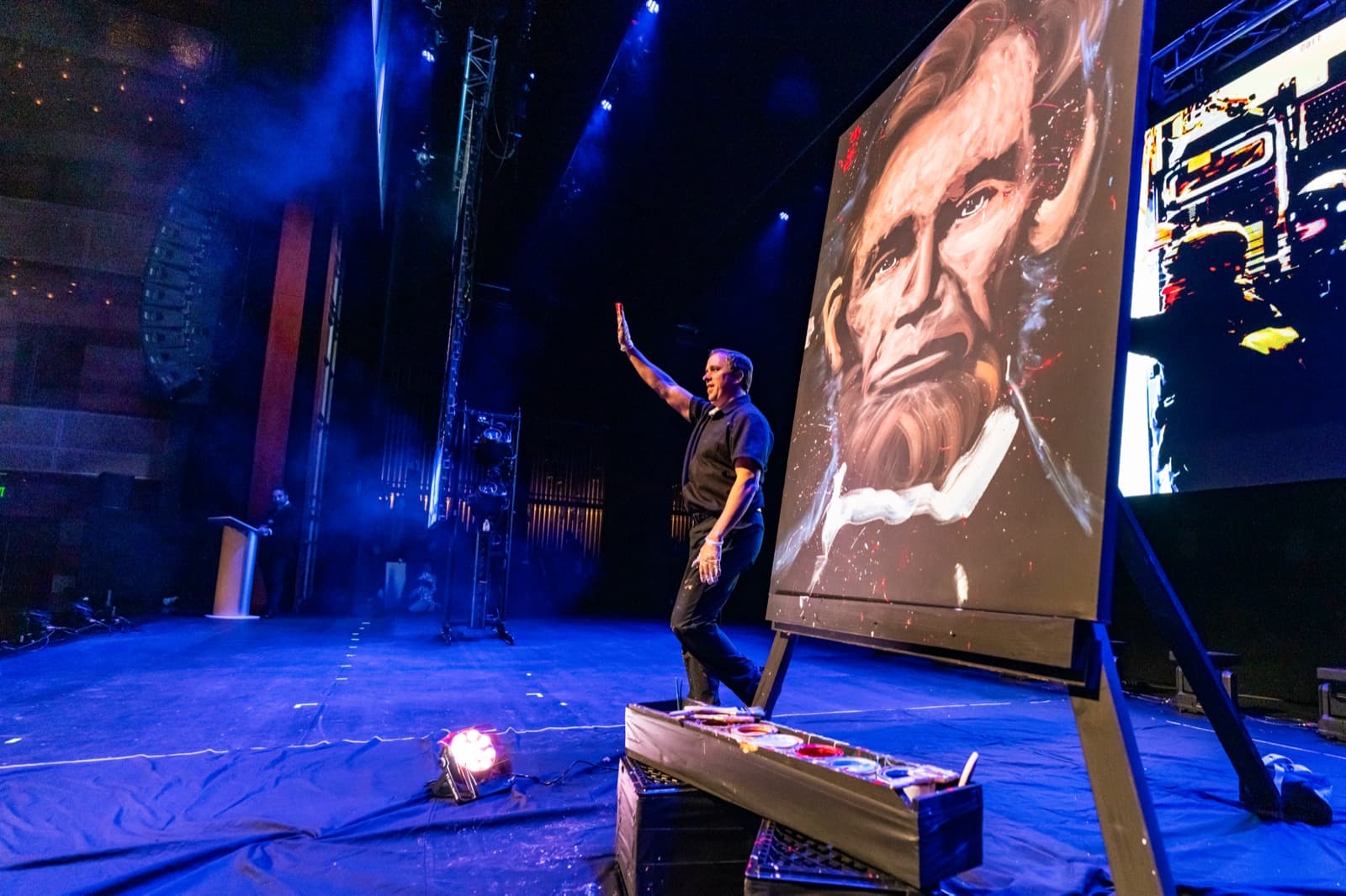 Warrior Rising speaker at a podium under blue stage lighting.