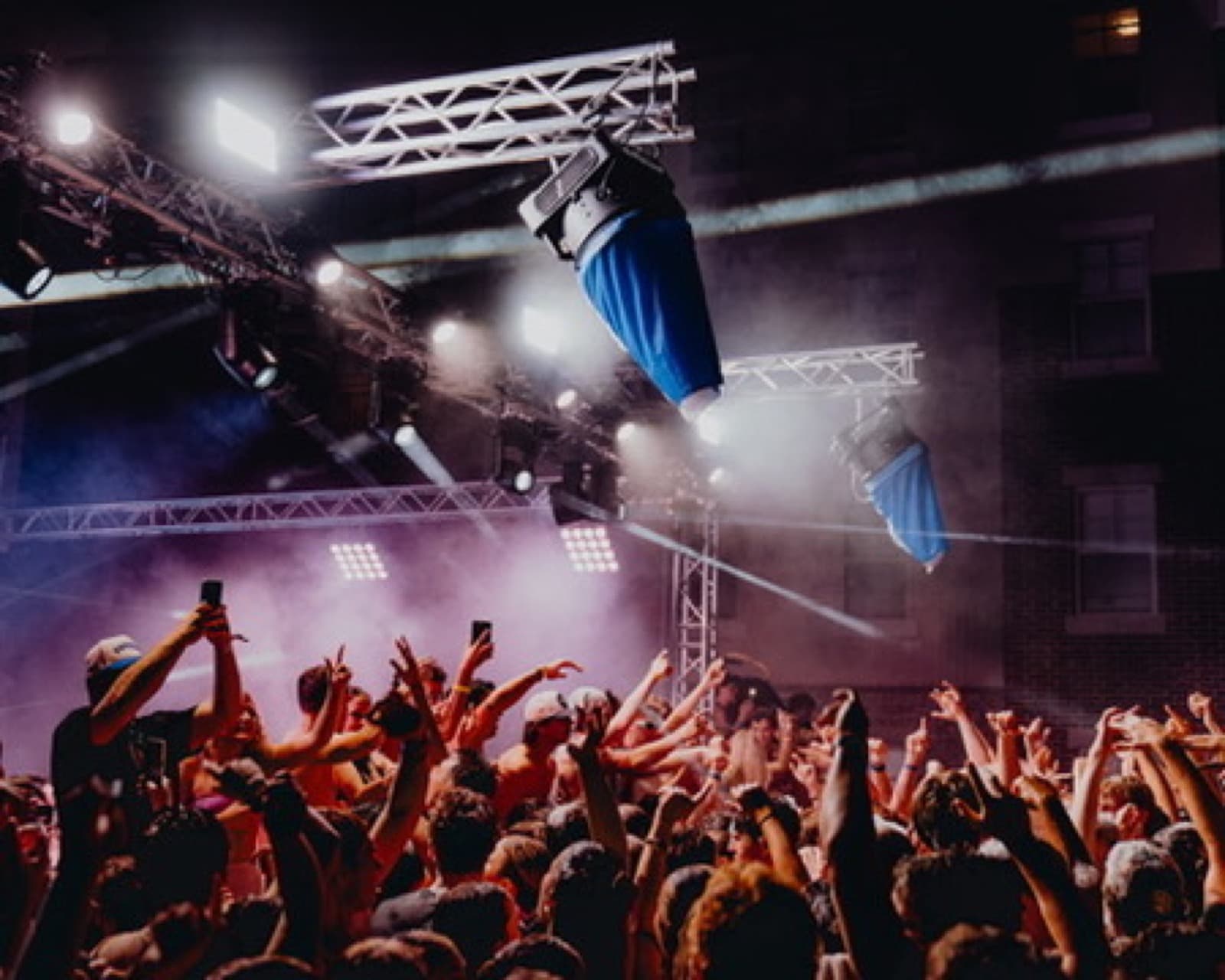 Party crowd with hands raised under bright blue stage lighting.