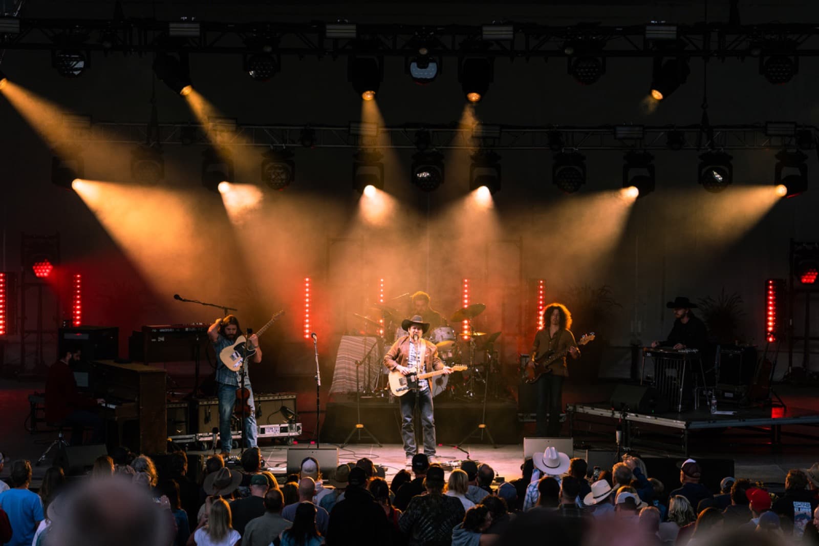 Outdoor concert stage with LED screens and blue lighting in front of a mountain audience.