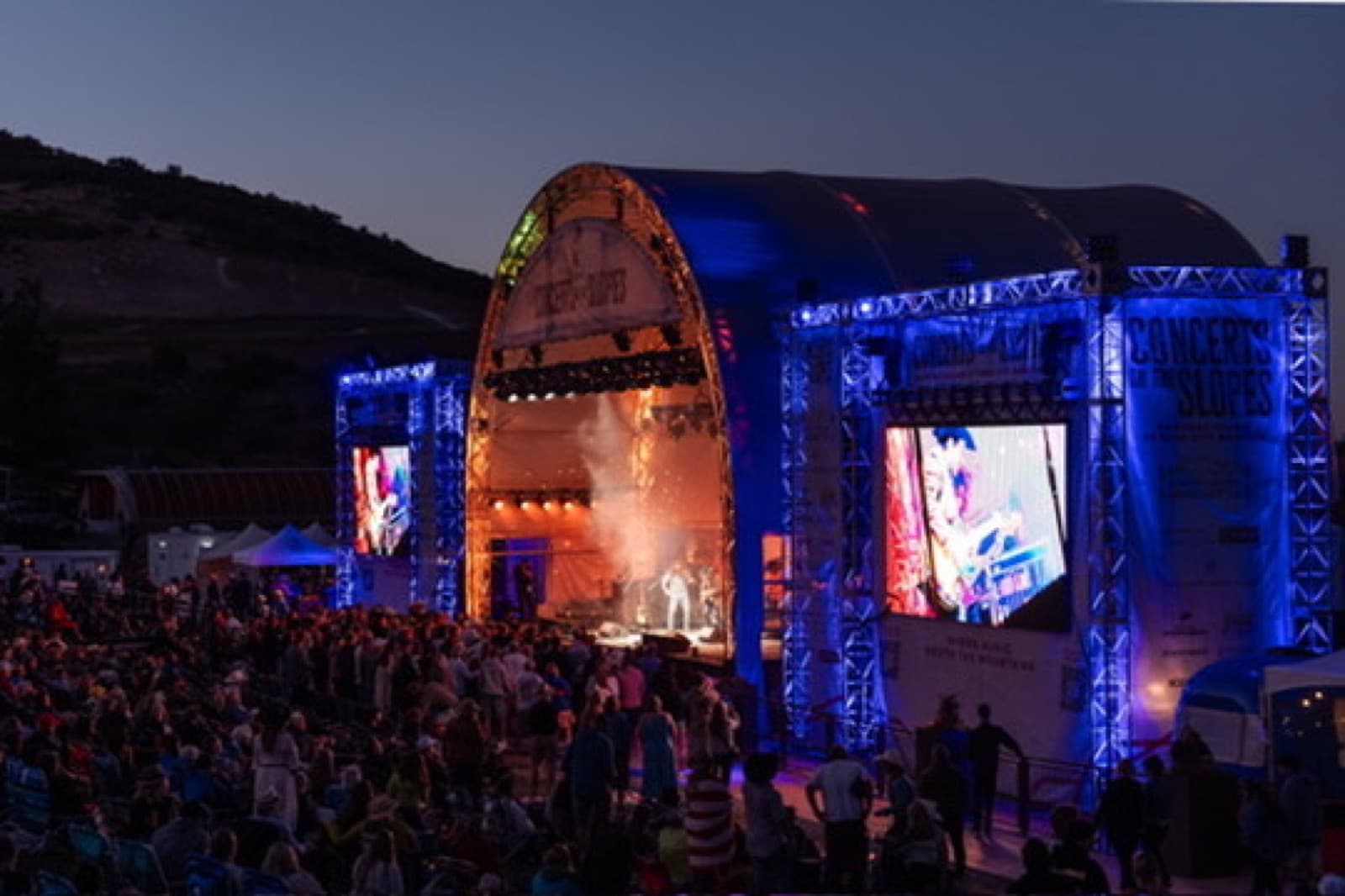 Concert lighting rig with amber beams over musicians on stage.