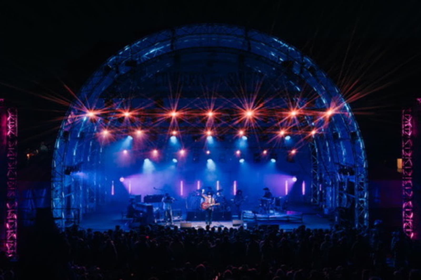 Wide outdoor stage view with video screens and blue stage wash.