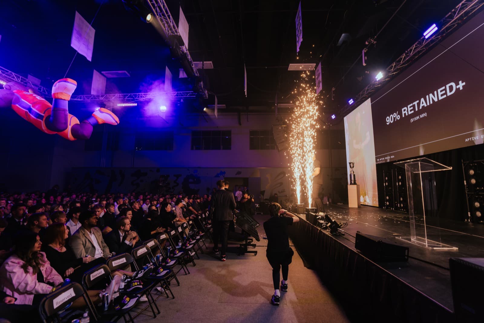 Aptive awards room with a full seated audience facing a large lit stage.