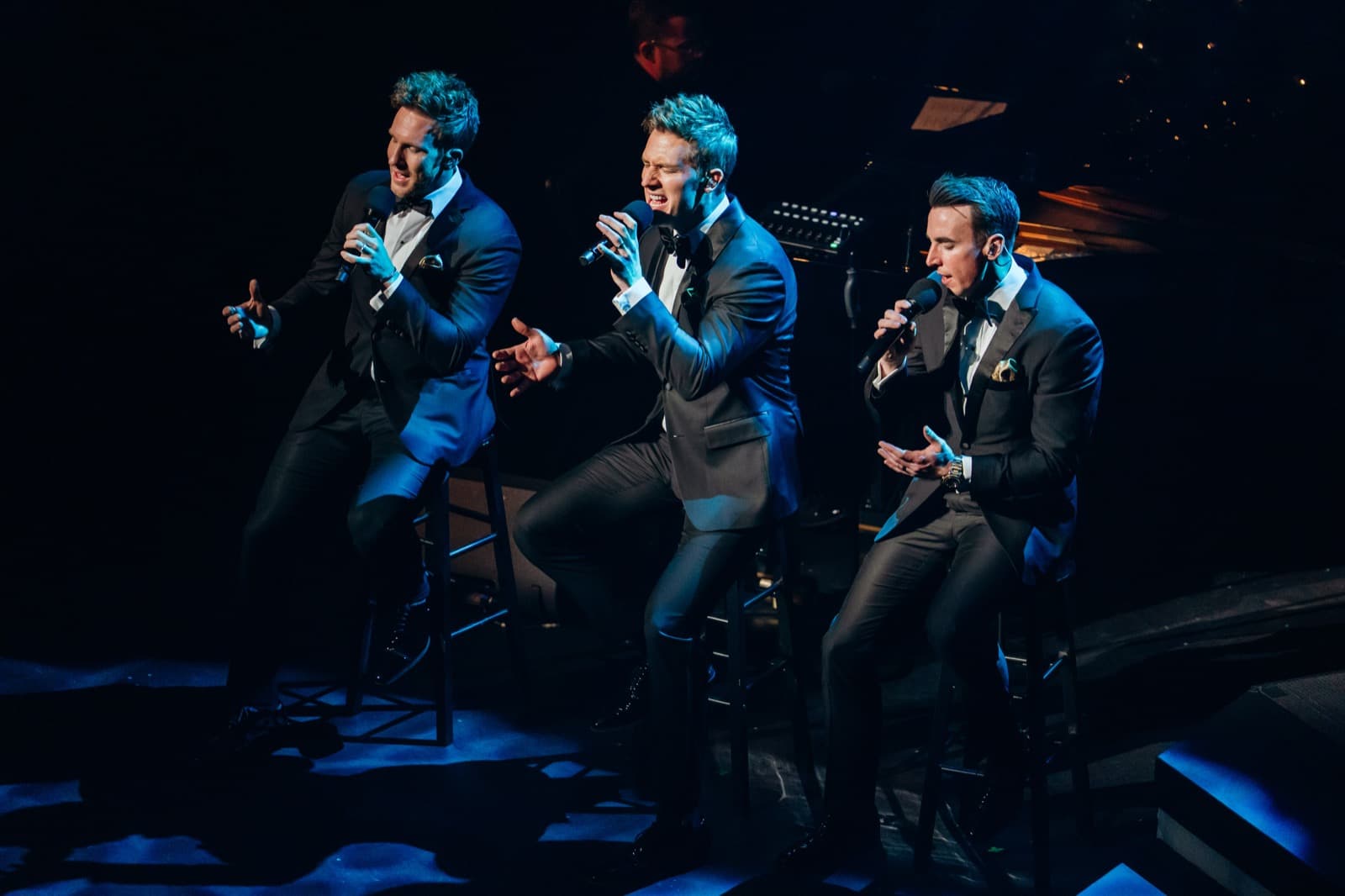 Three GENTRI vocalists performing together under blue lighting.