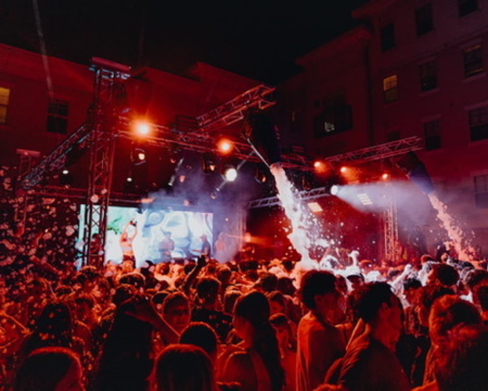 Private party crowd in warm red lighting facing a lit stage.