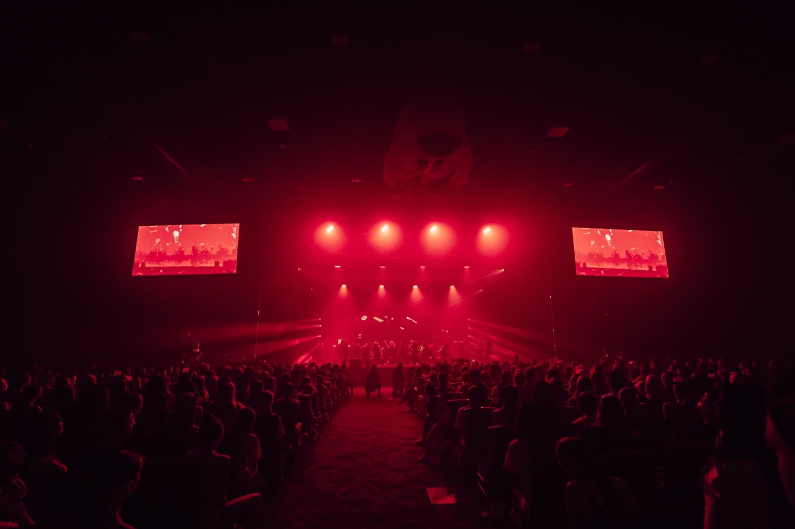 Five World stage under deep red lighting with audience silhouettes.