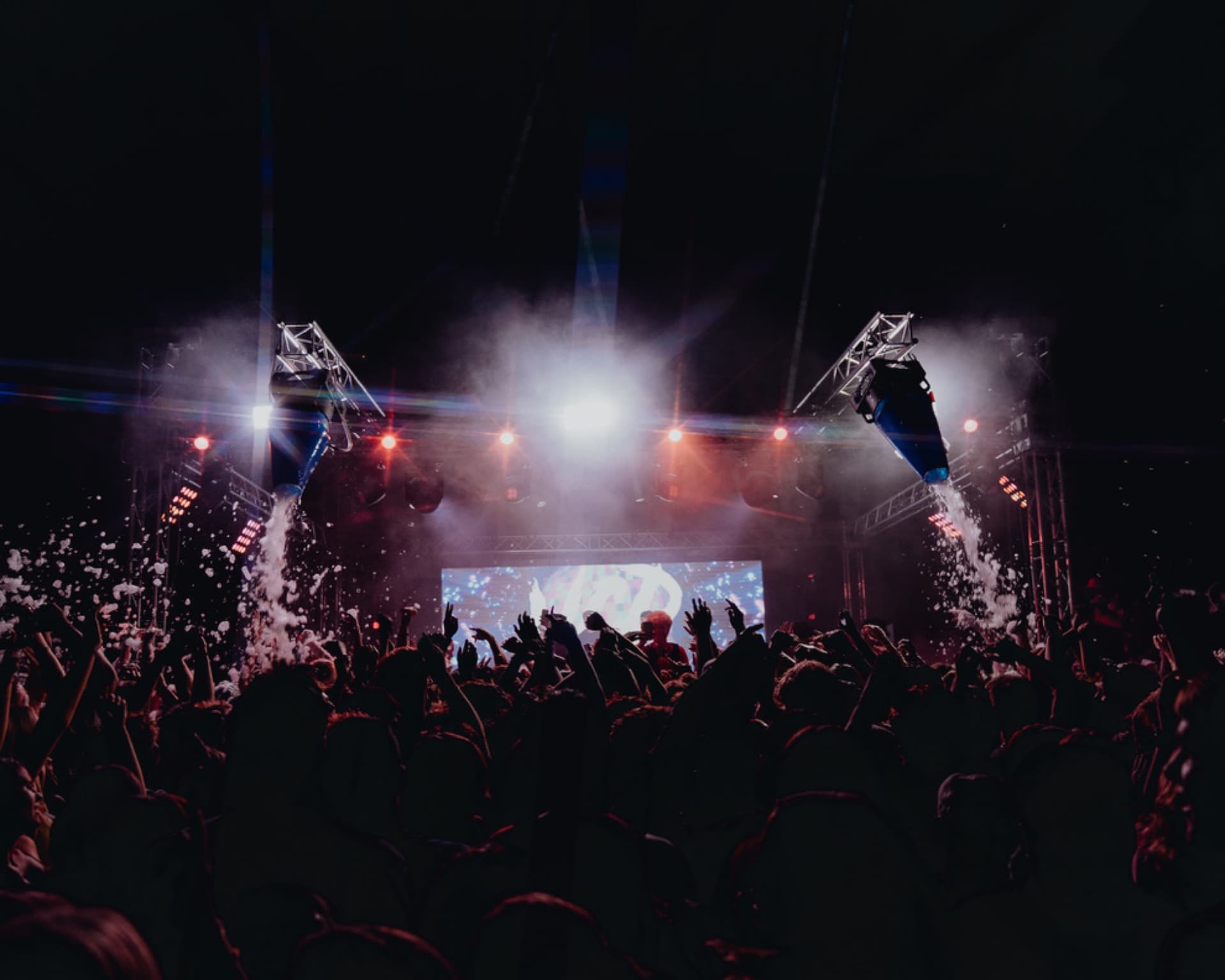 Private party crowd in front of a brightly lit concert-style stage with haze and beams.